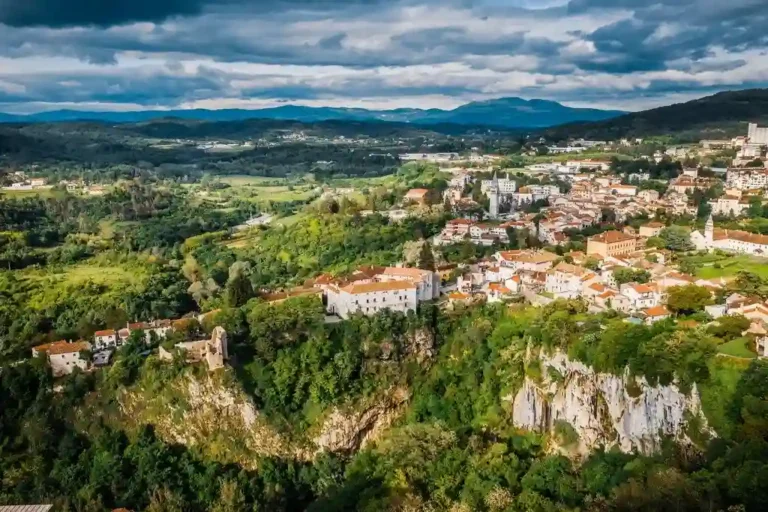 Pogled na pitoreskni gradić okružen zelenilom i brdima.