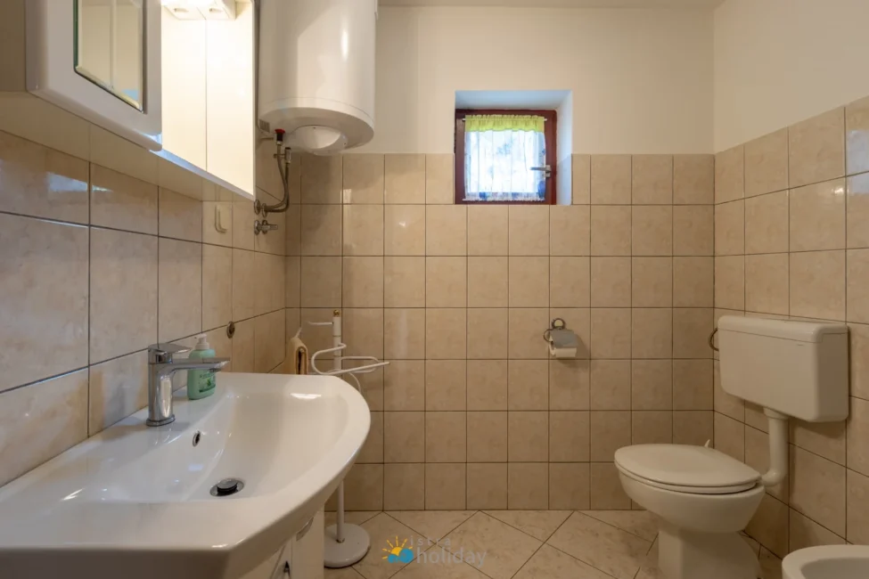 Tiled bathroom with sink, toilet, and small window