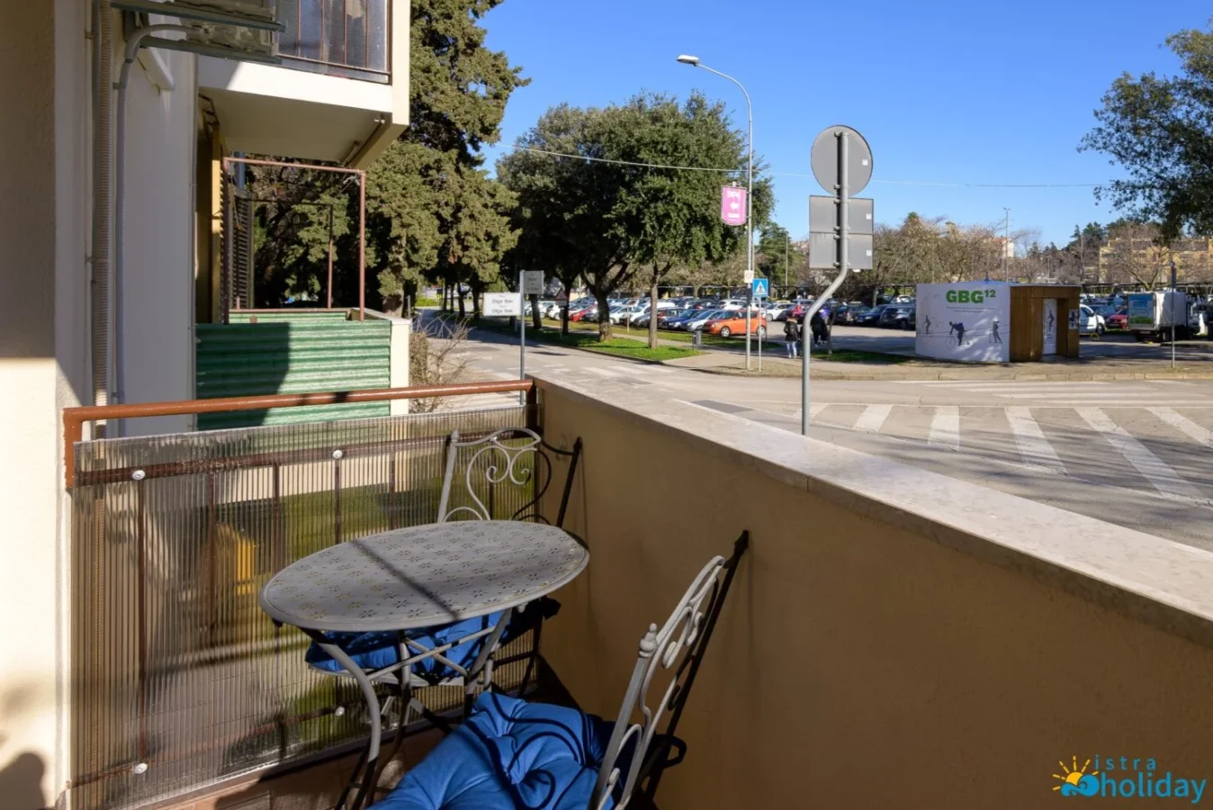 Sunny balcony overlooking a street and parking lot.