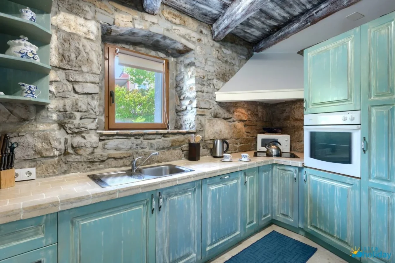 Rustic kitchen with stone walls and blue cabinets.