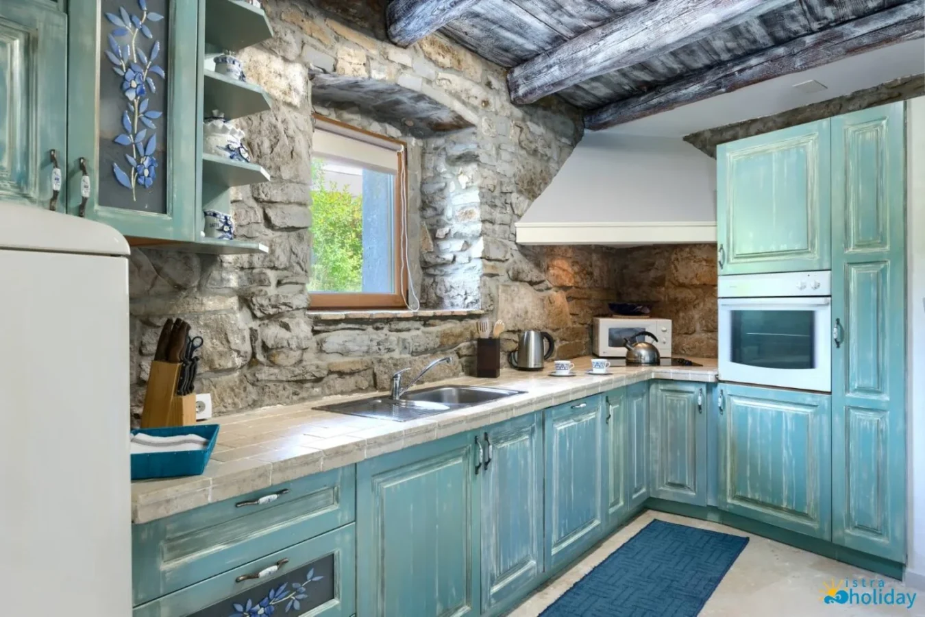 Rustic kitchen with stone walls and teal cabinets.