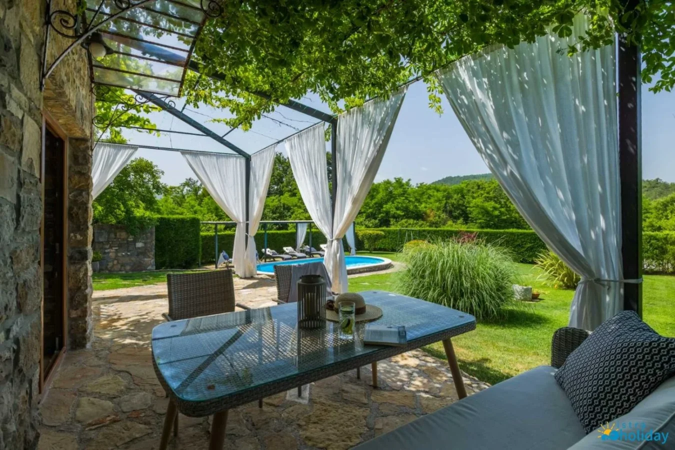 Shaded patio with curtains overlooking garden and pool.