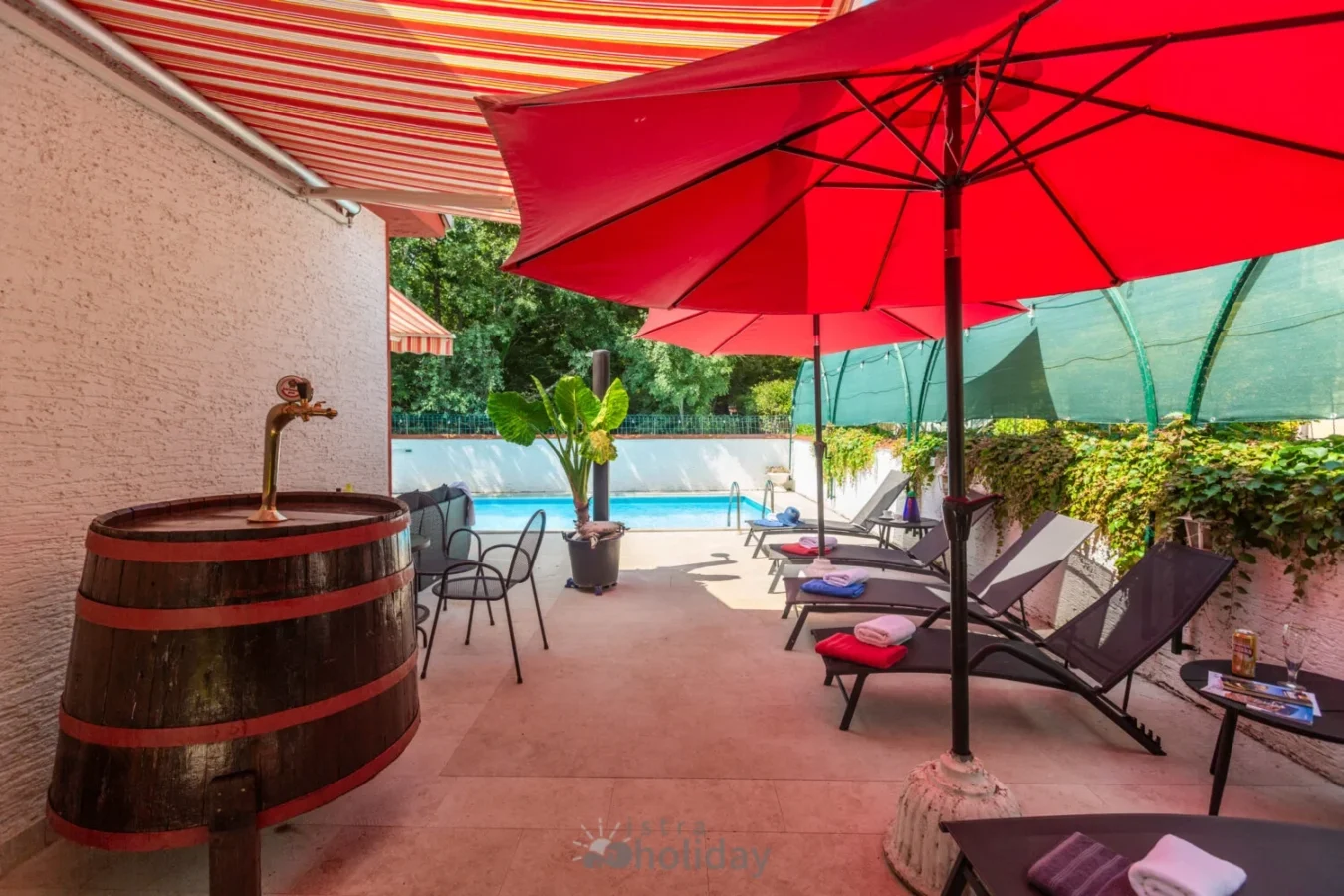 Patio with red umbrellas, pool, and lounge chairs.