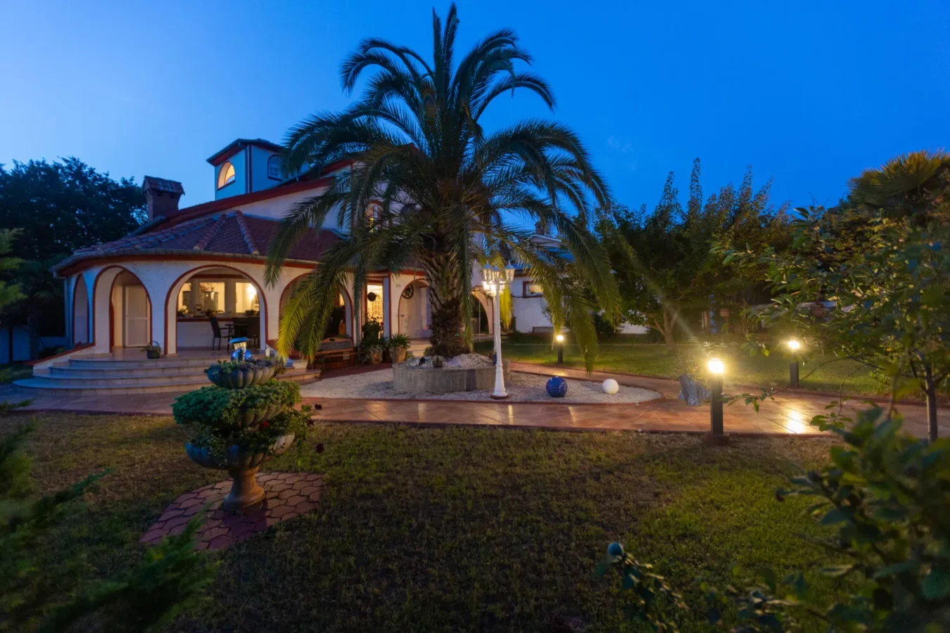 Peaceful evening garden with lights and palm tree.