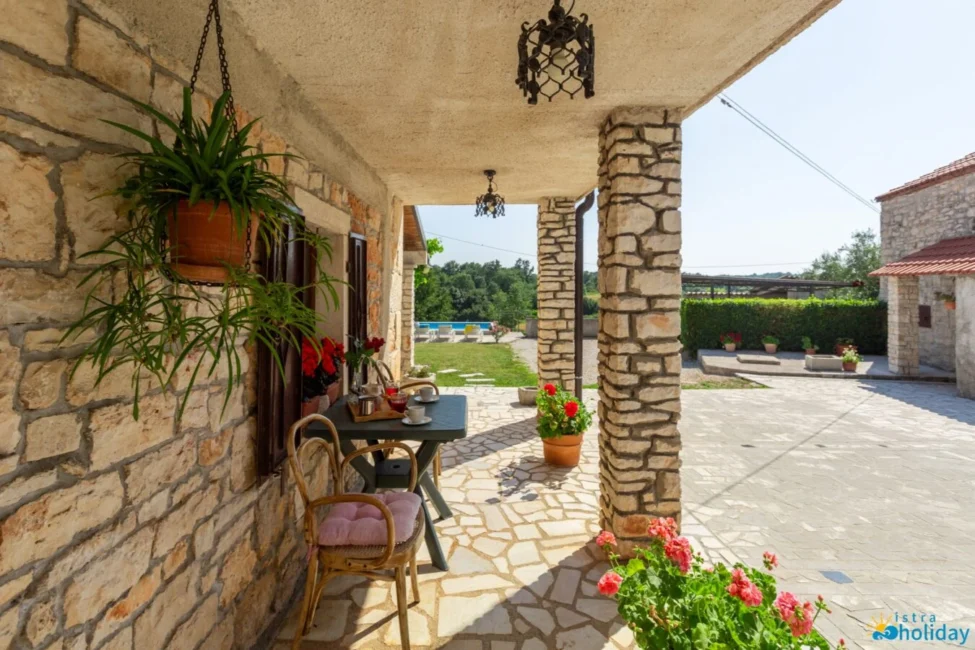 Rustic stone patio with potted plants and chairs.