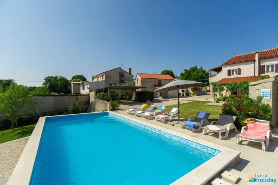 Outdoor pool with sun loungers and houses nearby.