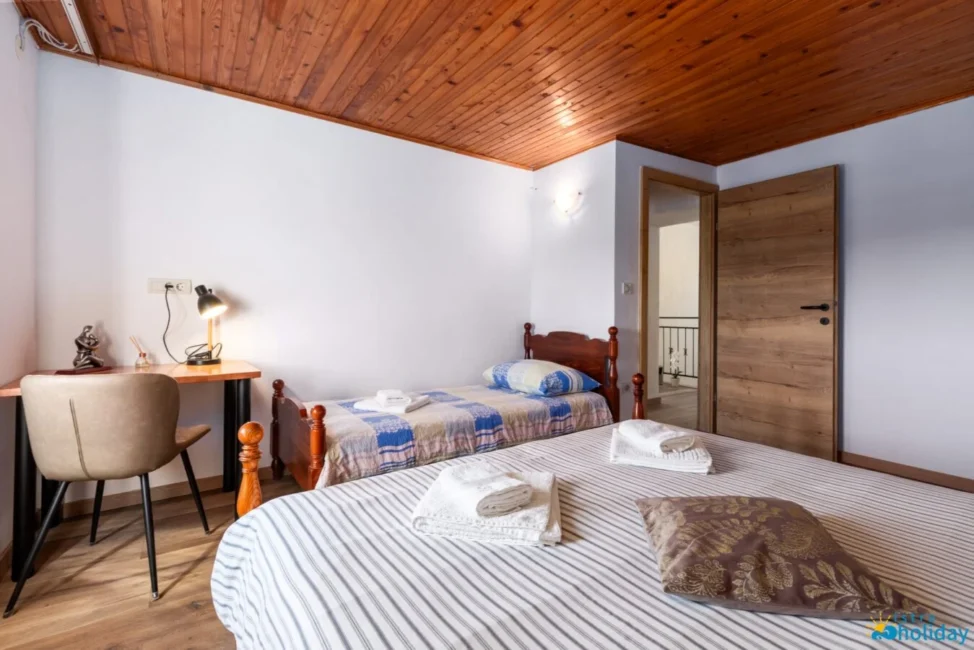 Cozy bedroom with two beds and wooden ceiling.