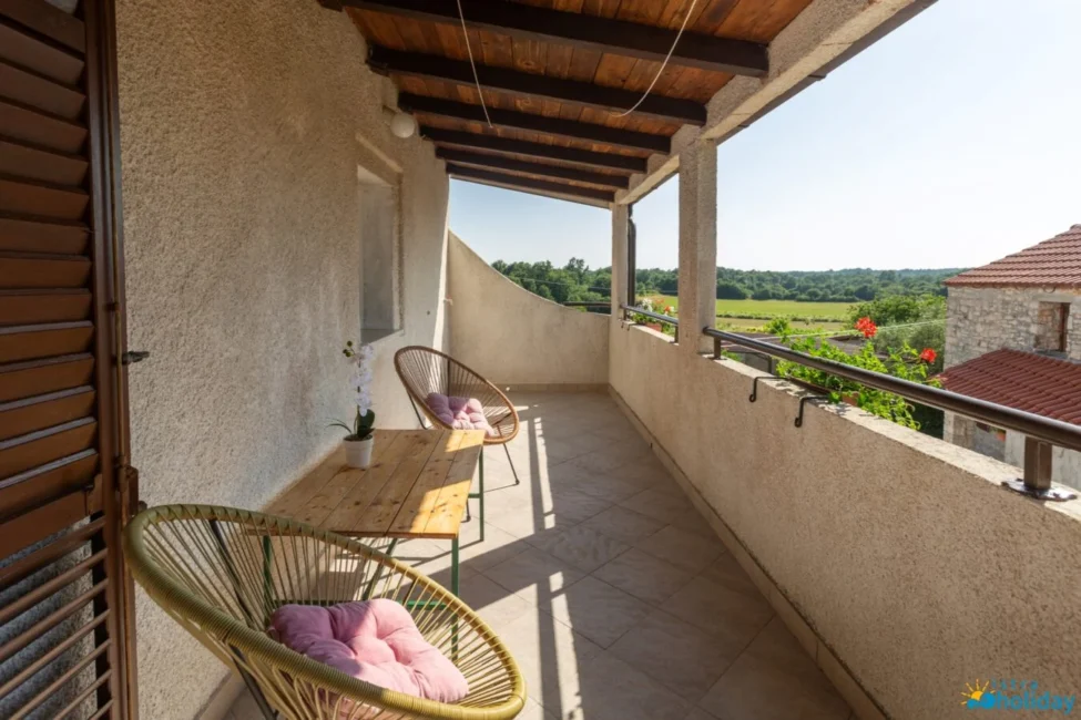 Sunny balcony with chairs and table overlooking garden.