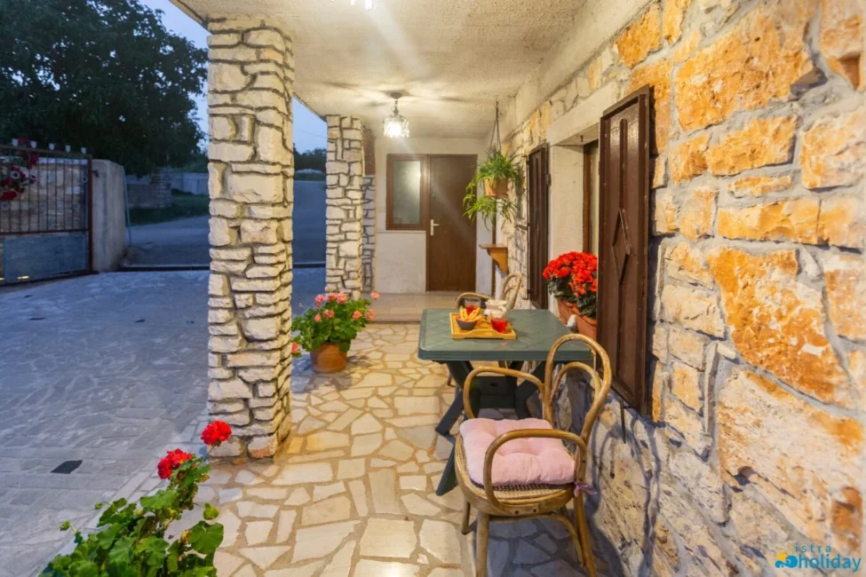 Stone porch with table, chairs, and flowers at dusk.